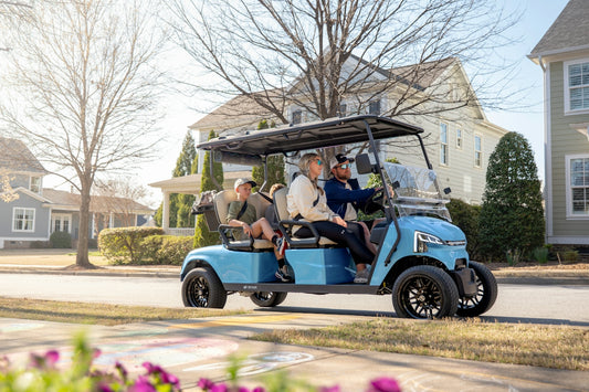 Four people ride a blue golf cart through a neighborhood