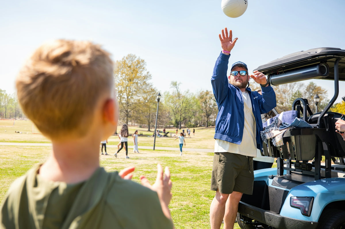 A man and boy playing volleyball near a golf cart