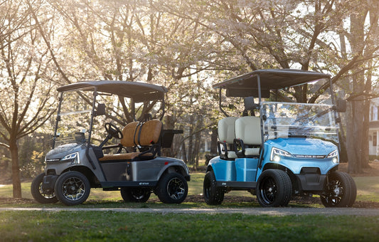 Two golf carts, one grey and one blue, parked outdoors.