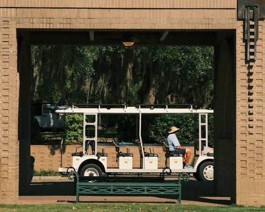 Person in straw hat drives white golf cart through archway