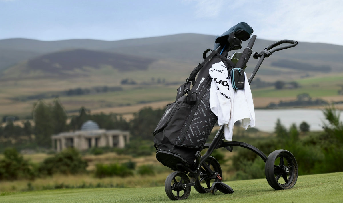 A golf bag on a push cart on a green course with rolling hills