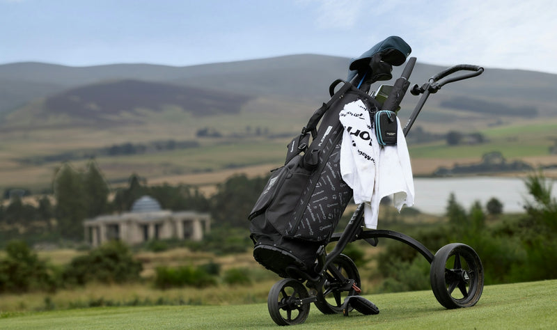 A golf bag on a push cart on a green course with rolling hills