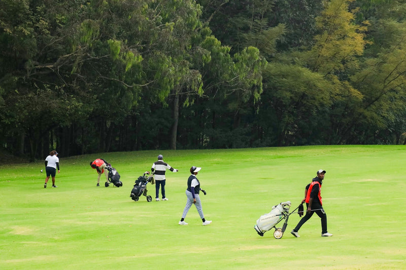 People walking across a green golf course with bags and clubs