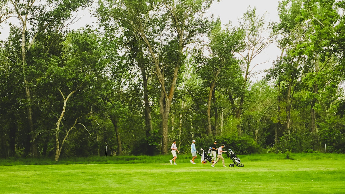 A group of people walking with golf bags across a green course